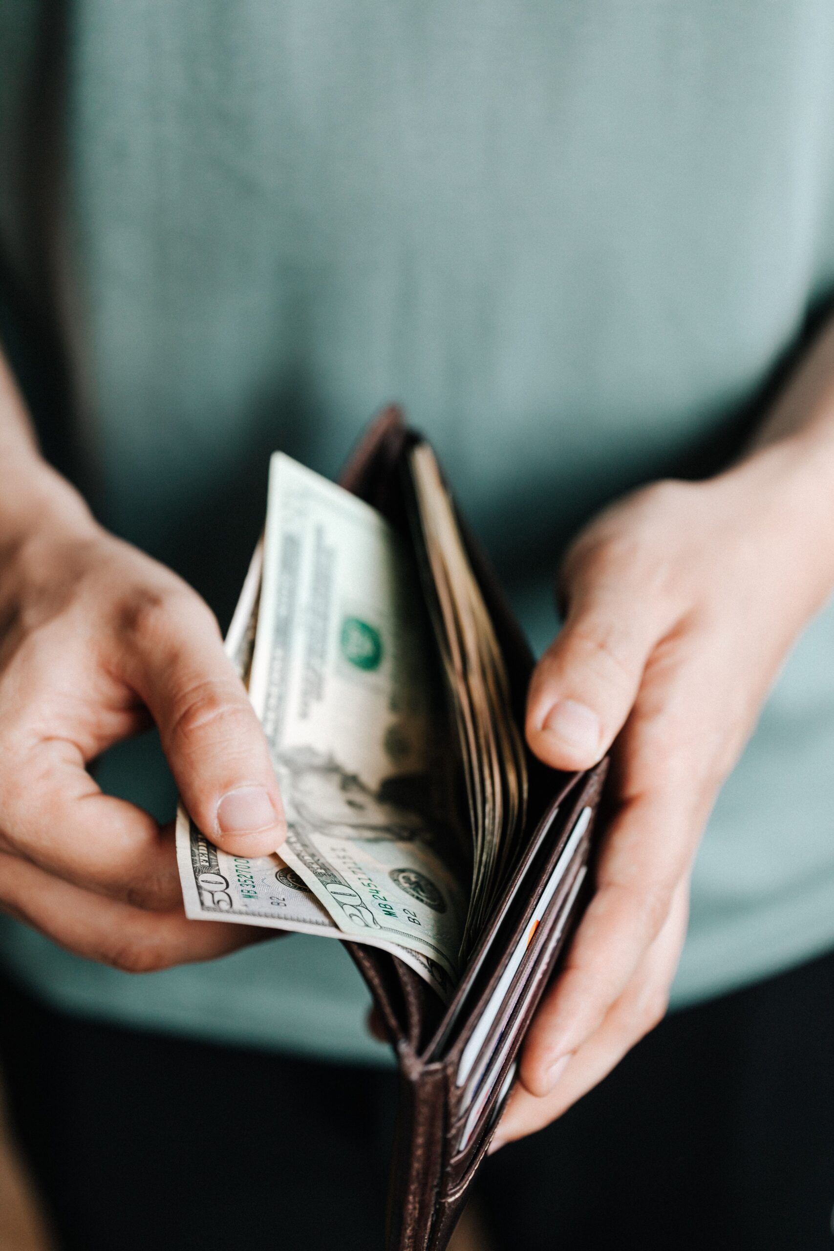 From above of crop unrecognizable man in casual outfit holding wallet with banknotes getting dollars up