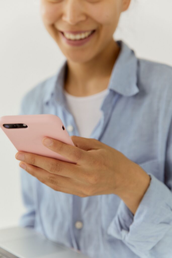 Close-up of a woman smiling while holding a pink smartphone indoors. Casual and friendly atmosphere.